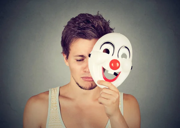 Молодой грустный человек снимает клоунскую маску — стоковое фото