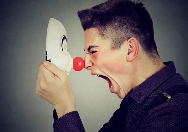 Perfil lateral homem irritado gritando com máscara de palhaço feliz — Fotografia de Stock