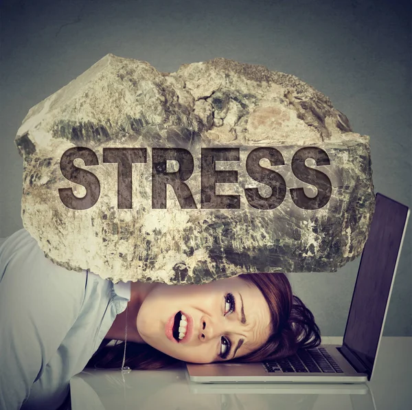 Stressed woman with head squeezed between laptop and a rock — Stock Photo, Image