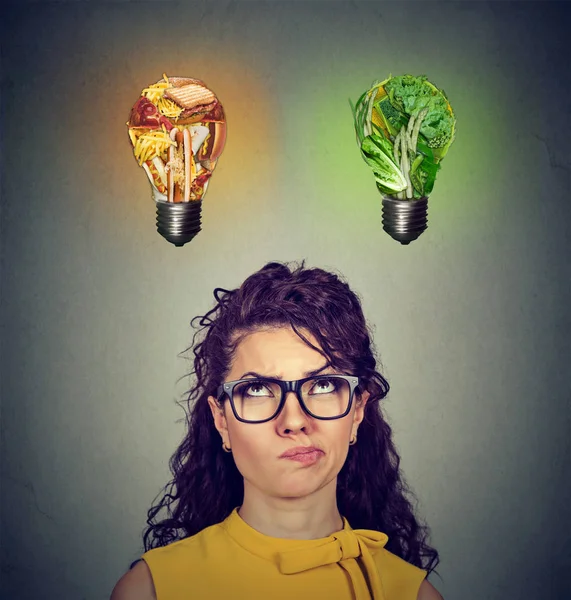 Donna pensando guardando il cibo spazzatura e verdure verdi lampadina — Foto Stock