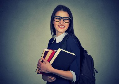 Bir sırt çantası taşıyan ve kitap yığını tutan gülümseyen öğrenci 