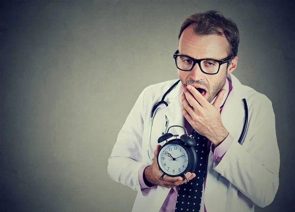 Sonolento, médico exausto segurando despertador, bocejo, cansado após o dia ocupado — Fotografia de Stock