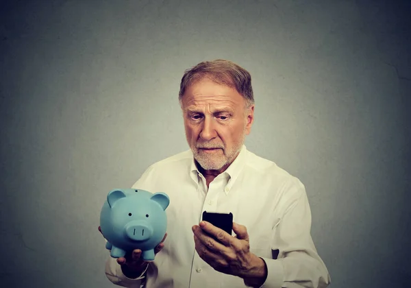 Besorgter Mann blickt auf sein Handy mit Sparschwein — Stockfoto