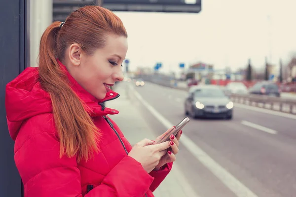 Happy woman calling a taxi with a smartphone app standing along the road — Stock Photo, Image