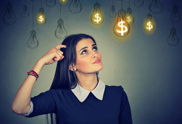 Думающая молодая женщина смотрит вверх на долларовую идею лампочки над головой — стоковое фото