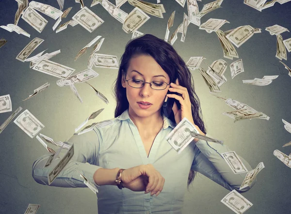 Businesswoman looking at wrist watch, talking on mobile phone under cash rain. — Stock Photo, Image