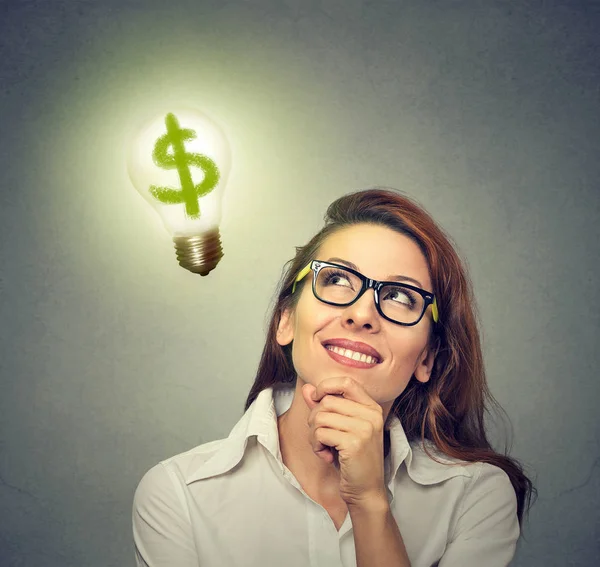 Деловая женщина смотрит на лампочку с табличкой доллара внутри — стоковое фото