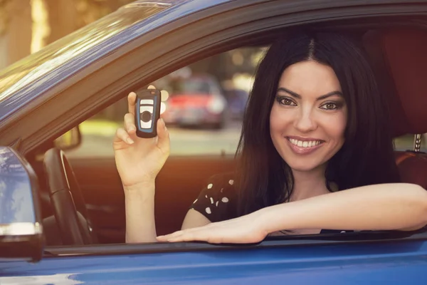 Smiling woman sitting in her new blue car showing keys — Stock Photo, Image