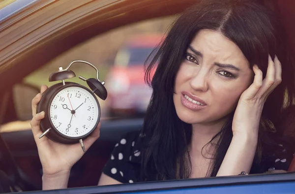 Worried woman inside car showing alarm clock running late to work — Stock Photo, Image