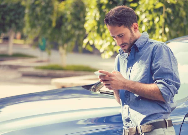Человек, стоящий у машины и переписывающийся по мобильному телефону — стоковое фото