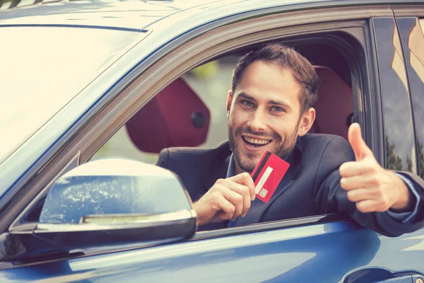 Счастливчик в своей новой машине показывает кредитку, показывающую большие пальцы вверх — стоковое фото