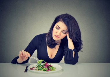 Displeased young woman eating green leaf lettuce tired of diet restrictions  clipart