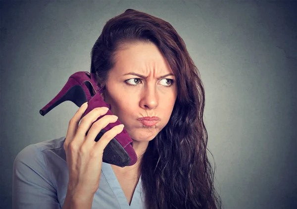 Расстроенная женщина держит туфлю на высоком каблуке в руке, как телефон — стоковое фото