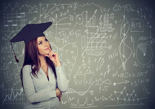 Mulher na formatura cap pensando sobre a educação, equilíbrio da vida profissional em pé por informações gráficos blackboard fundo — Fotografia de Stock