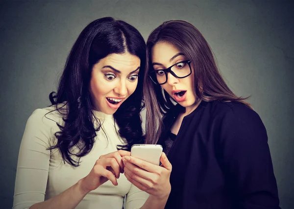 Zwei verblüffte Mitbewohnerinnen, die online auf einem Smartphone Angebote ansehen. — Stockfoto