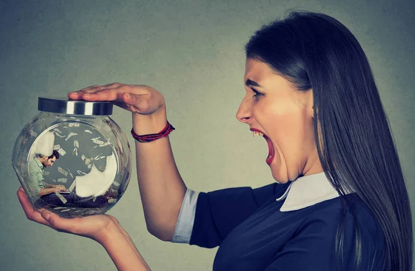 Angry woman holding a glass jar with a man working on laptop trapped inside — Stock Photo, Image