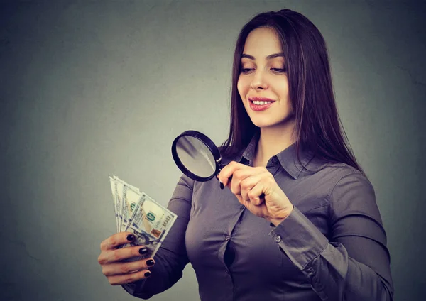 Woman looking at one hundred dollar bills through magnifying glass — Stock Photo, Image