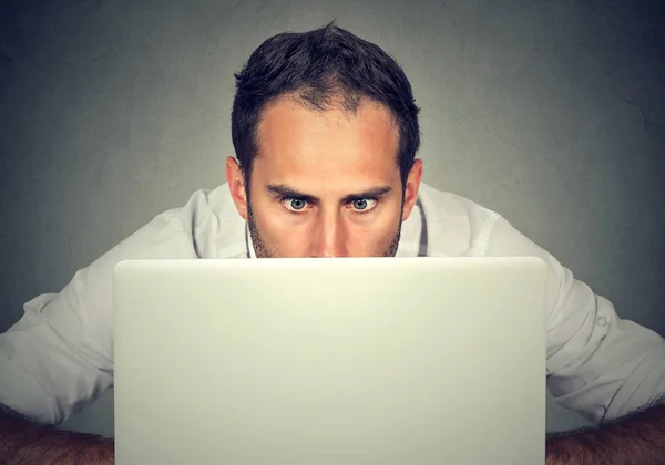 Людина ховається за ноутбуком, дивлячись на екран з шокованим виразом обличчя — стокове фото
