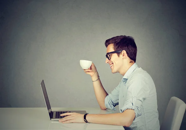 Счастливый человек, работающий на ноутбуке, пьет кофе — стоковое фото