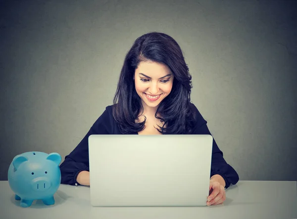 Businesswoman working with laptop computer sitting at desk with piggy bank — Stock Photo, Image