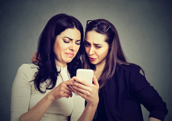 Två upprörd vänner kvinnor visar på linje innehåll på en smart telefon — Stockfoto