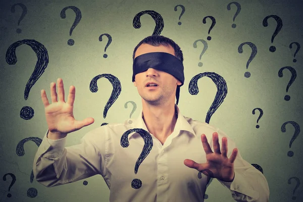 Blindfolded man stretching his arms out walking through many question marks — Stock Photo, Image