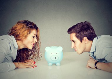 Finances in divorce concept. Wife and husband can not make settlement looking at piggy bank sitting at table looking at each other with hatred clipart