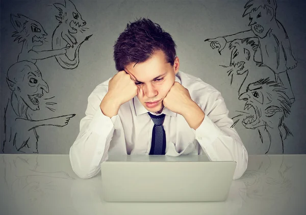 Maus homens maus apontando para o cara estressado sentado à mesa com computador portátil — Fotografia de Stock