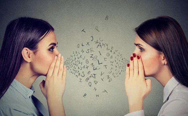 Two women whispering a gossip secret to each other with alphabet letters in-between — Stock Photo, Image