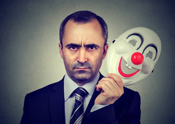 Angry business man taking off happy clown mask  