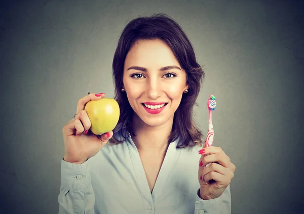 Smiling woman holding an apple and toothbrush — Stock Photo, Image