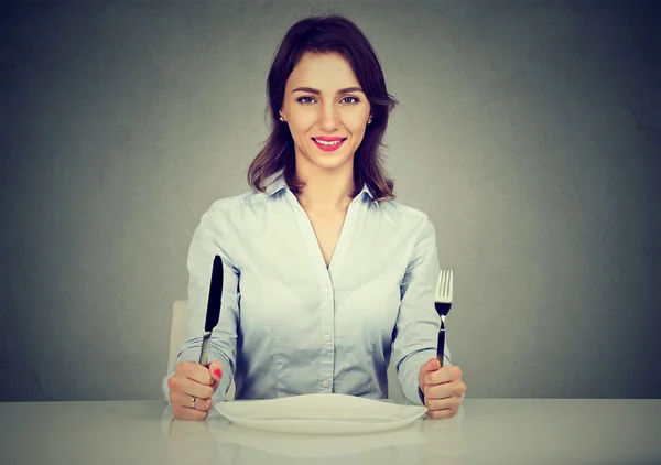 Happy woman with fork and knife sitting at table with empty plate — Stock Photo, Image