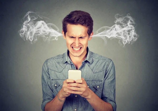 Angry man reading a text message on smartphone blowing steam coming out of ears — Stock Photo, Image
