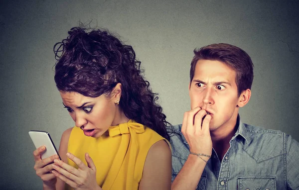 Podvádění přítel. Muž nervózně kousal nehty zároveň šokován přítelkyně čtení textových zpráv na svůj mobilní telefon — Stock fotografie