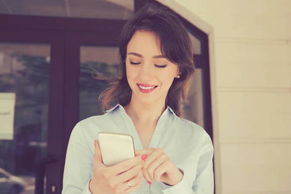 Donna guardando il suo telefono cellulare e sorridente in piedi fuori condominio complesso . — Foto Stock