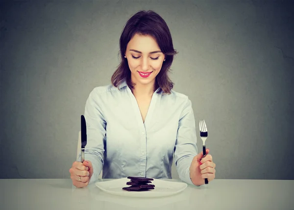 Frau sitzt lächelnd am Tisch und blickt auf ihren Wüstenschokoladenkuchen — Stockfoto