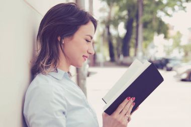 Dışarıda kitap okuyan genç bir kadın.