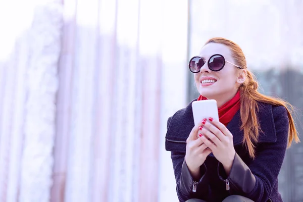 Beautiful woman sitting at the street holding her mobile phone smiling — Stock Photo, Image