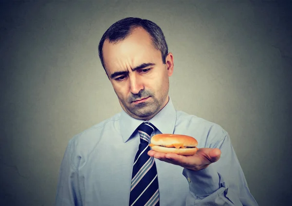 Vážnou zralý muž dívá na cheeseburger — Stock fotografie