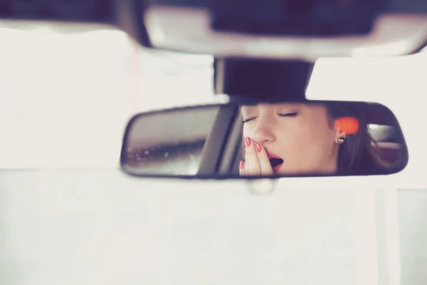 Vista trasera del espejo de una mujer bostezando soñolienta conduciendo su coche después de una larga hora en coche . — Foto de Stock