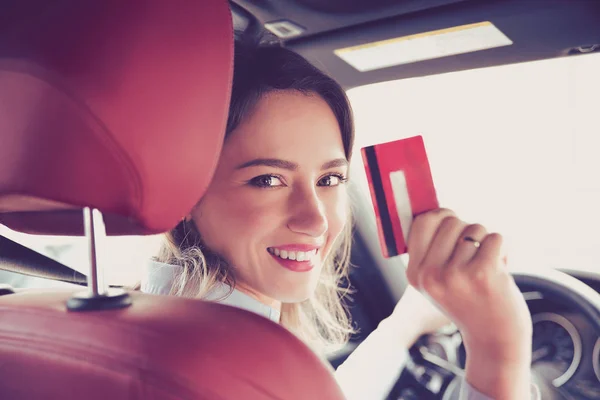 Szczęśliwa młoda kobieta siedzi wewnątrz jej nowy samochód wyświetlone karty kredytowej — Zdjęcie stockowe