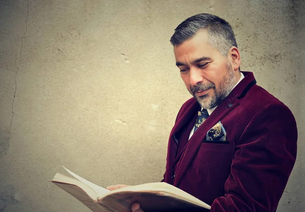 Ώριμος άνδρας διαβάζοντας ένα παλιό βιβλίο που στέκεται από ένα τσιμεντένιο τείχος σε εξωτερικούς χώρους — Φωτογραφία Αρχείου
