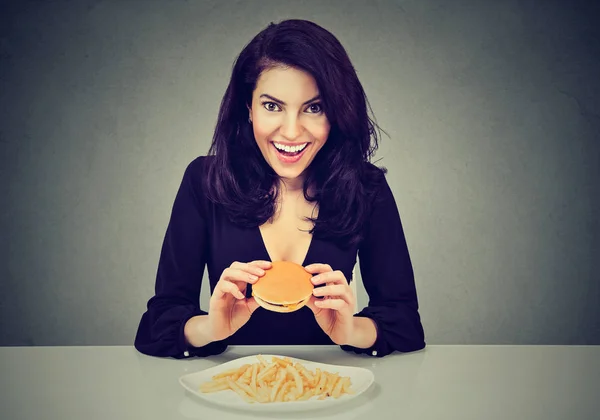 Le piace il fast food. Felice giovane donna mangiare cheeseburger e patatine fritte — Foto Stock