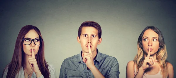 Secretive young people man and two women with finger to lips gesture — Stock Photo, Image