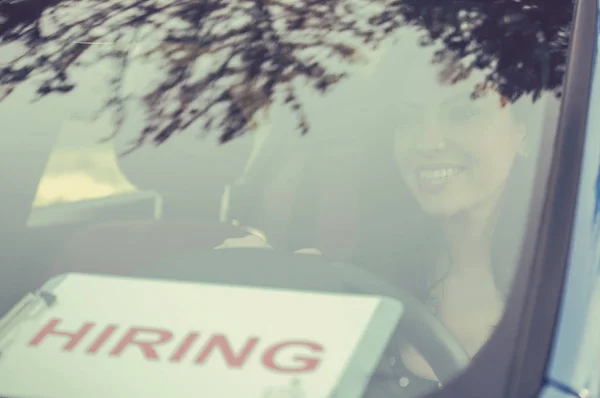 Счастливая молодая женщина водитель в своей машине с табличкой найма на лобовом стекле — стоковое фото