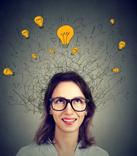 Young woman in glasses with many ideas light bulbs above head looking up — Stock Photo, Image