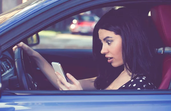 Mujer sorprendida distraída leyendo un mensaje en el celular conduciendo un coche — Foto de Stock