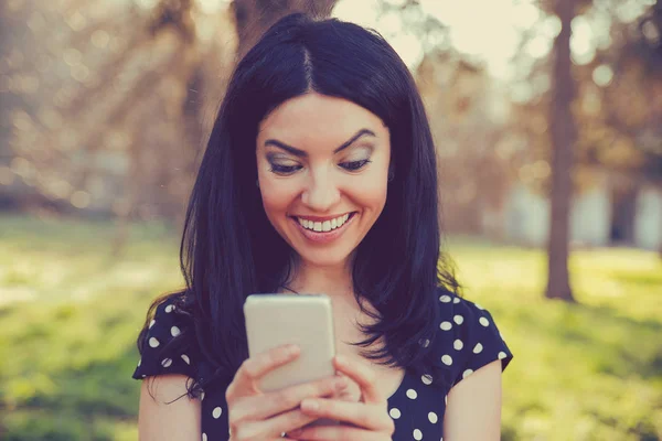 Чарівна молода жінка, використовуючи мобільний телефон, на фоні літнього парку — стокове фото