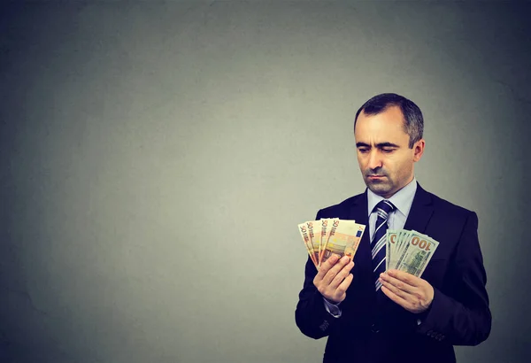 Un uomo d'affari attento che guarda alle banconote in euro e in dollari — Foto Stock