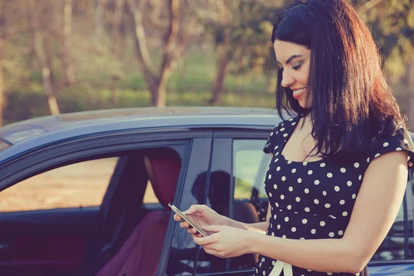 Успешная молодая женщина, стоящая у машины, пишет смс на мобильный телефон — стоковое фото